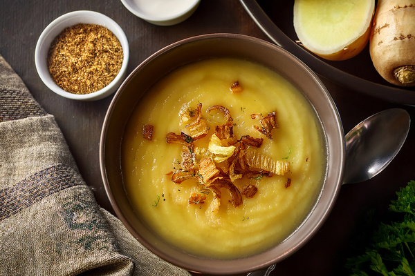 KI generiert: Cremige Suppe in einer Schüssel mit knusprigen Zwiebeln und Gewürzen, daneben Gewürze und Gemüse.