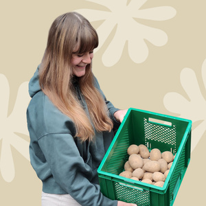 KI generiert: Eine Frau hält einen Wirsingkohl lächelnd vor einer Wand aus grünen Behältern. Der Hauptinhalt des Bildes ist die Präsentation des Kohls in einem fröhlichen Kontext.