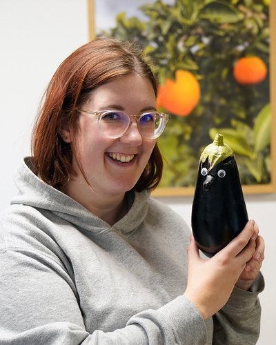 KI generiert: Eine Person hält eine Aubergine mit aufgeklebten Augen und lächelt.