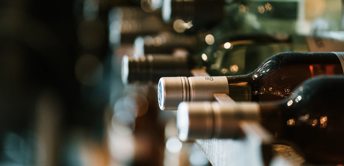 KI generiert: Das Bild zeigt Weinflaschen, die in einem Regal liegen, hauptsächlicher Fokus ist auf den Flaschenhälsen. Das Szenario vermittelt eine Atmosphäre von Eleganz und Weinlagerung.